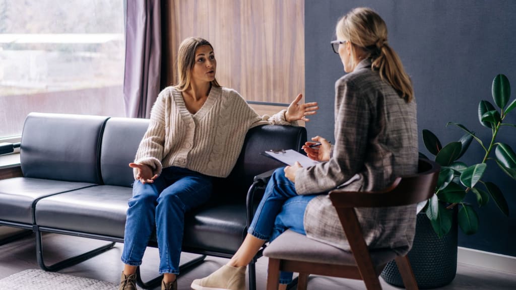 Two women sitting on a couch talking to each other.